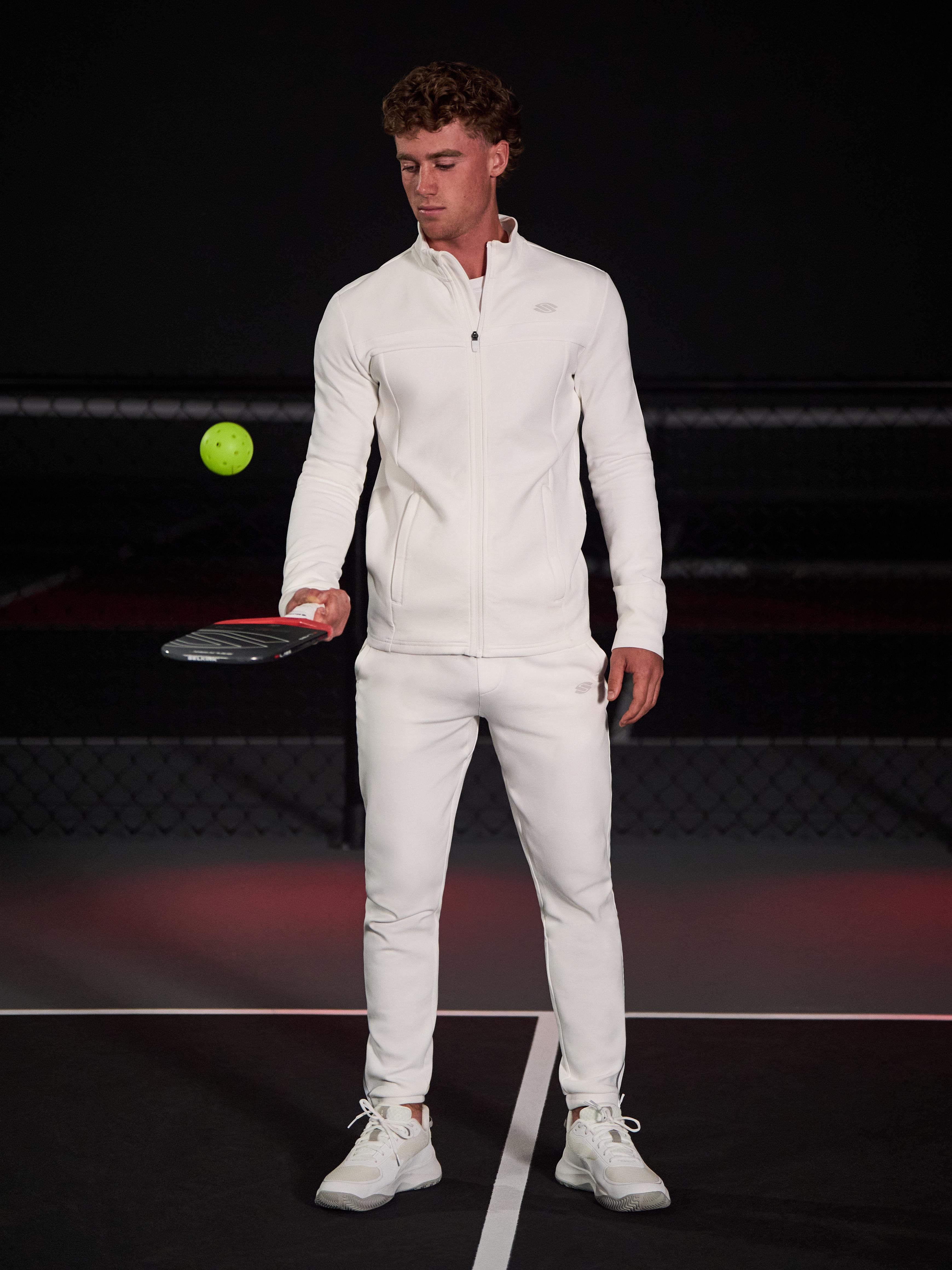 Model wearing Men’s Pro Line Knit Jogger and jacket, holding a pickleball paddle with a ball in the air.