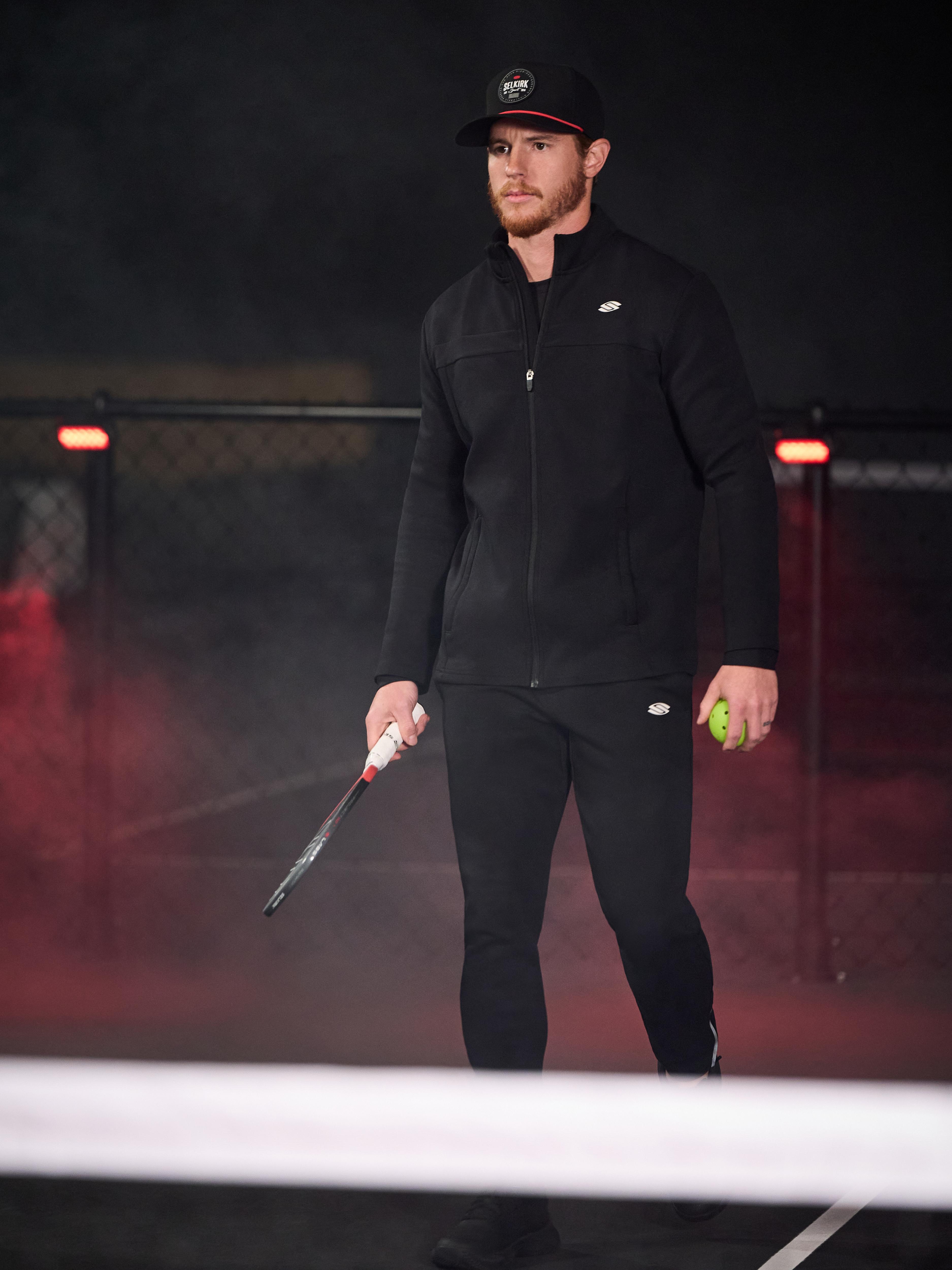 Man wearing Men's Pro Line Full Zip Jacket, holding a pickleball paddle and ball on a court
