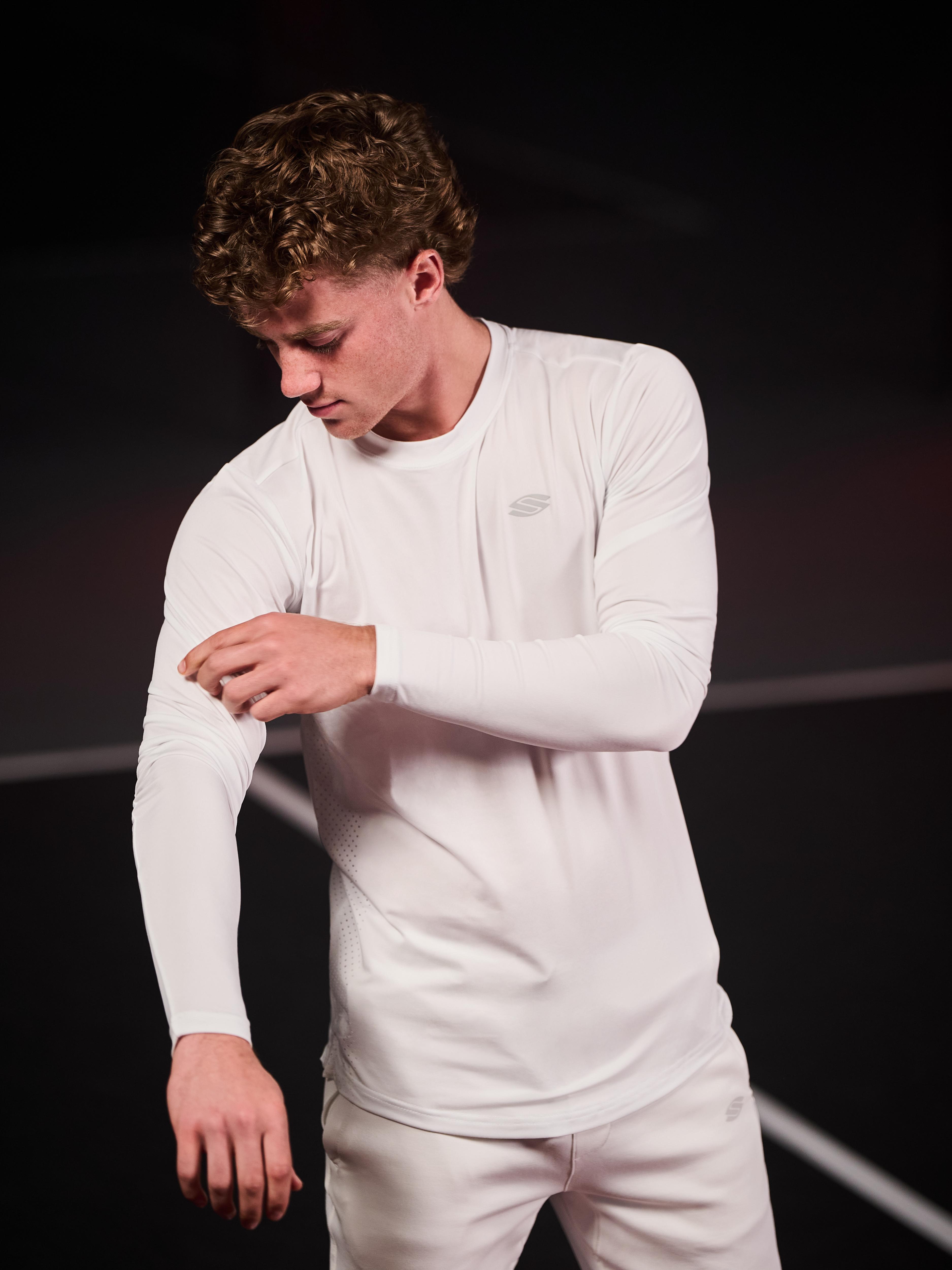 Model wearing a white long sleeve athletic shirt, adjusting the sleeve.