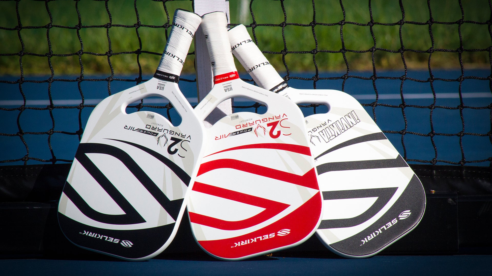 Three Vanguard Power Air pickleball paddles in red and white colors, displayed against a net.