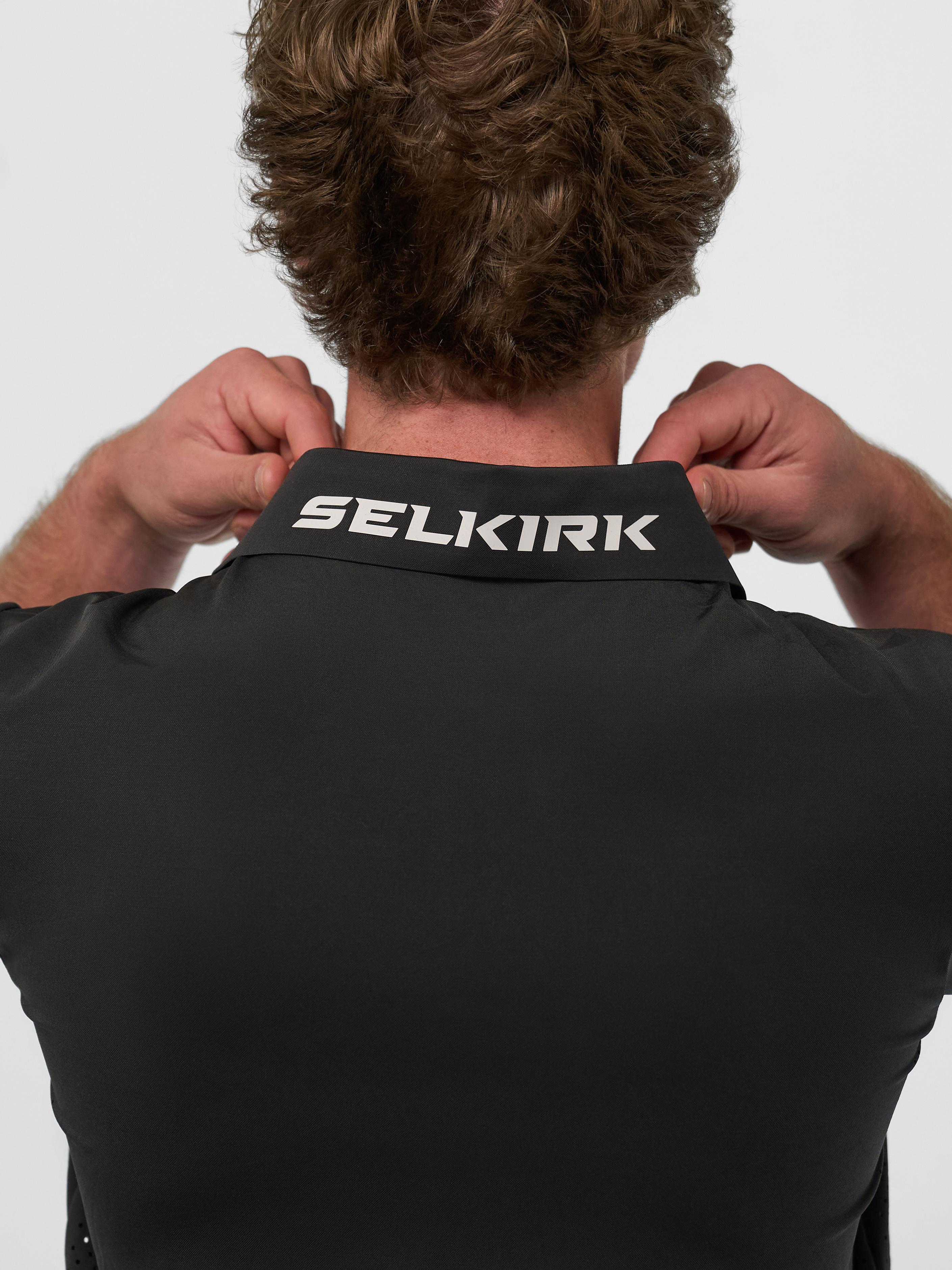 Back view of a man adjusting the collar of a black Selkirk Performance Polo with logo.