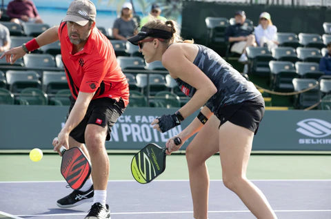 A man and woman playing pickleball, preparing to hit the ball.