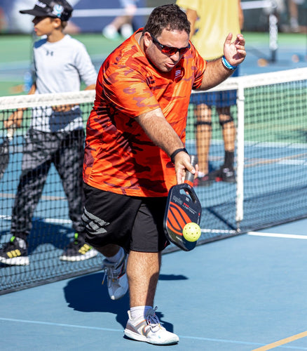 A player in an orange shirt returning a pickleball on a court.