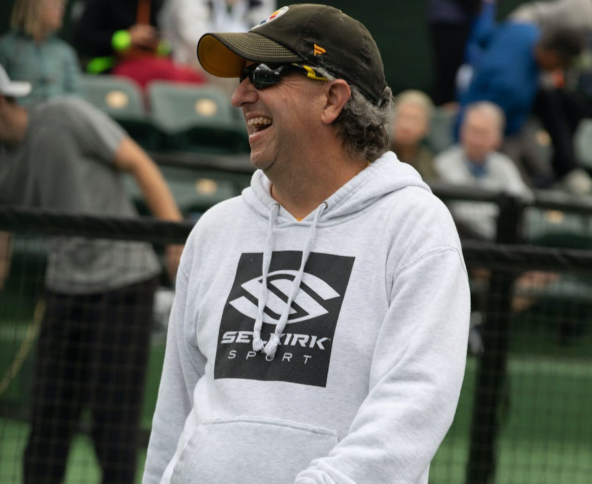 Smiling man in a hoodie playing pickleball outdoors
