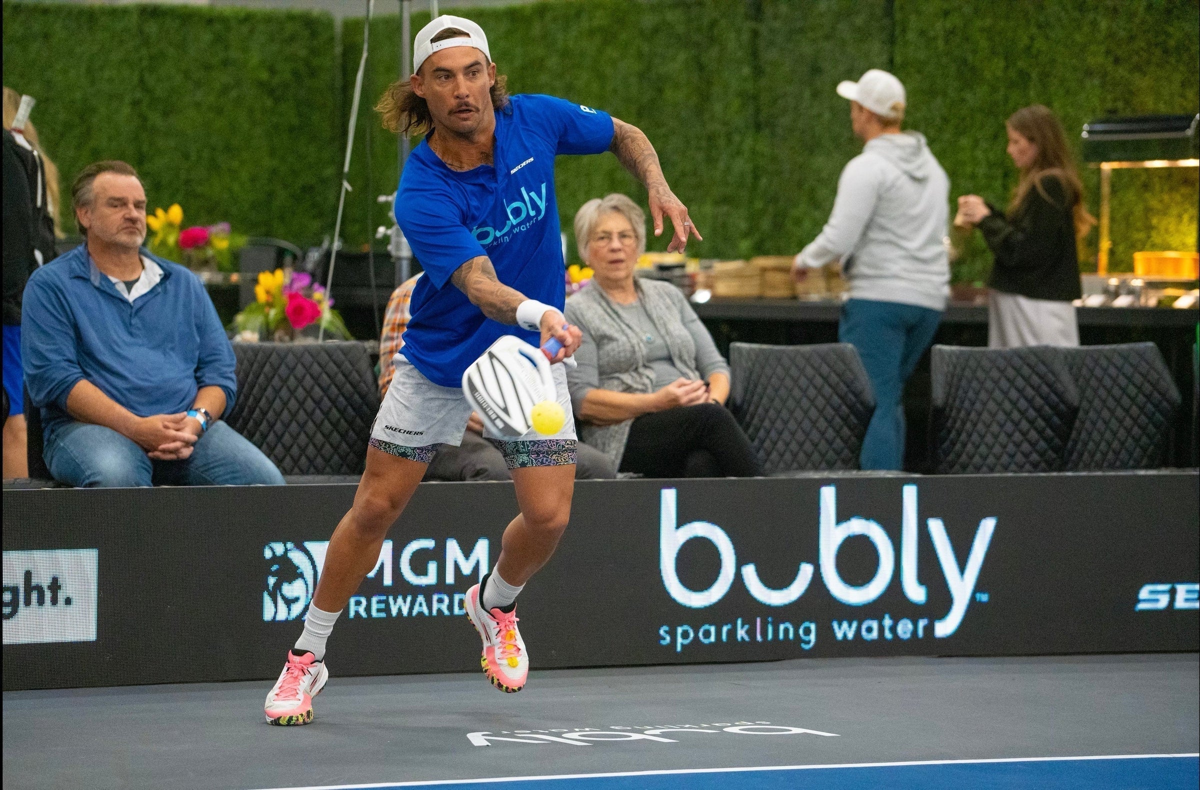 A player in a blue shirt hitting a pickleball with 'bubly sparkling water' logo visible.