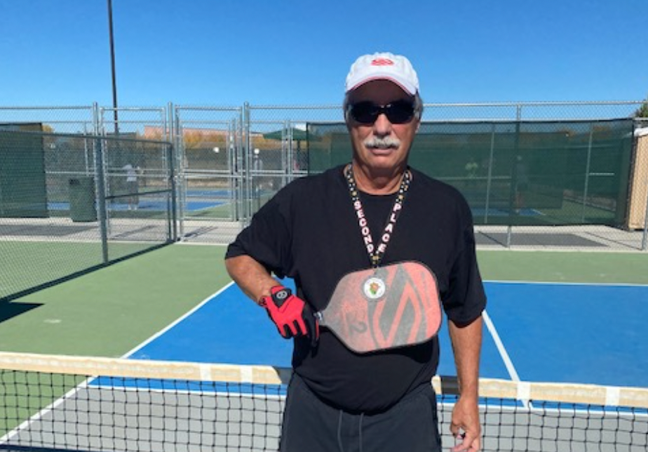 A man in a black shirt and red glove holding a pickleball paddle on a court.