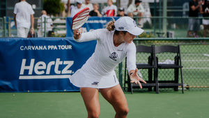A female pickleball player in action, wearing a white outfit and preparing to hit the ball on the court during the PPA tournament.