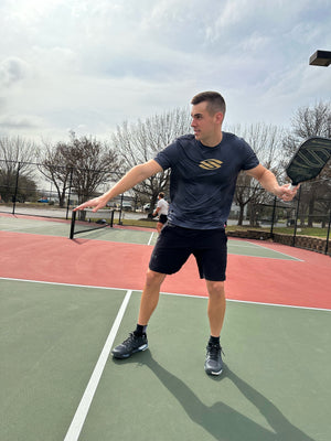 A male pickleball player in a black shirt preparing to hit a ball on a court.