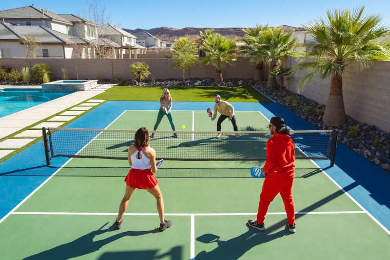 Four people play pickleball on an outdoor court beside a swimming pool
