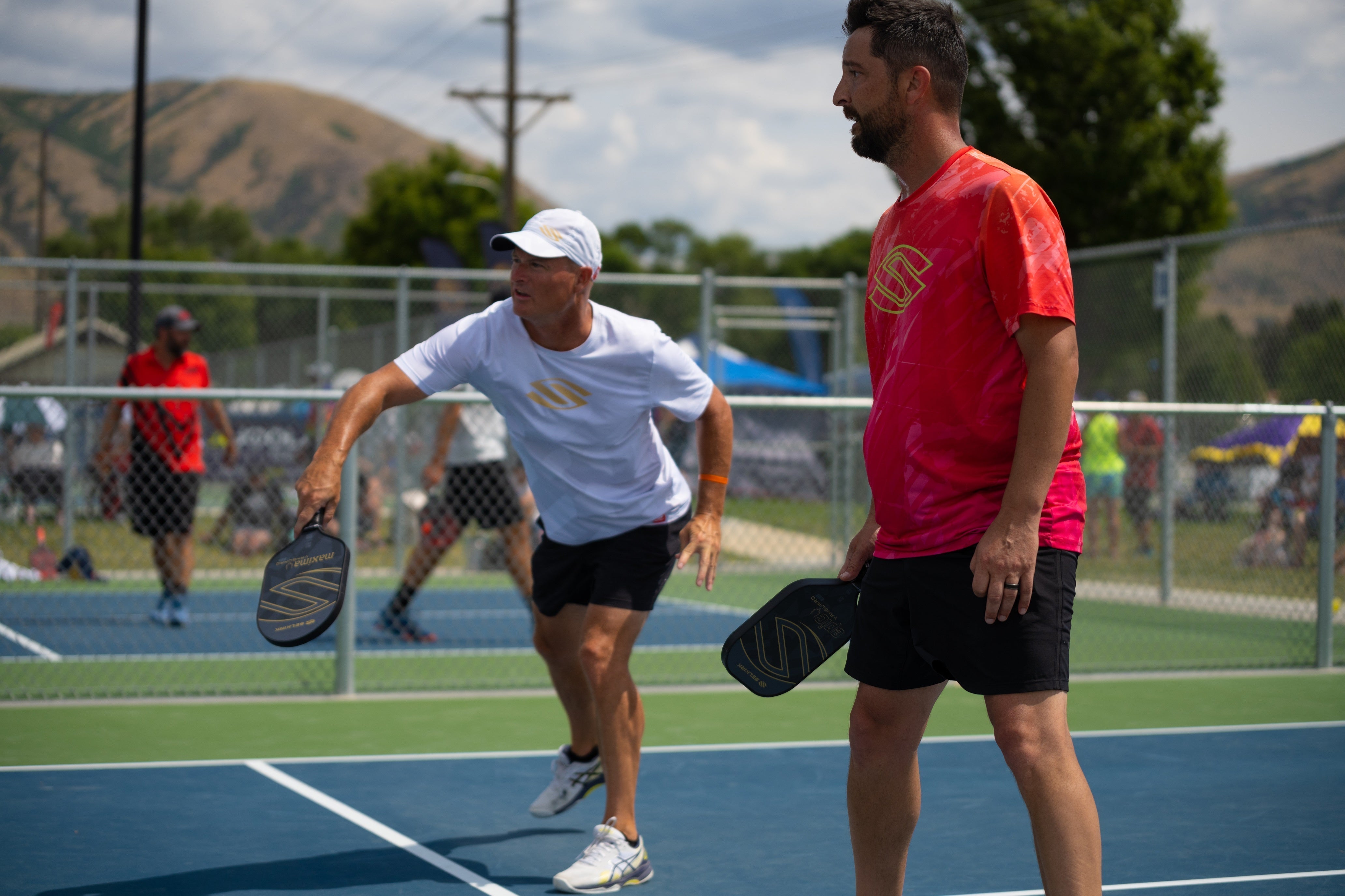 Two men playing pickleball on a court, one preparing to serve.