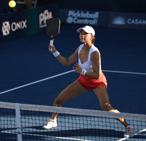 Female pickleball player preparing to hit a ball during a match on a blue court.