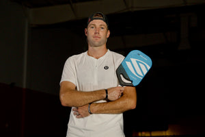 Jack Sock poses with a blue Luxx Control Air pickleball paddle while wearing a white shirt