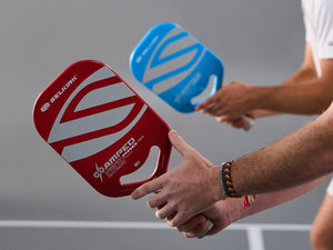 Close-up of two Selkirk Invikta Amped Pro pickleball paddles, red paddle foreground showing face graphics, blue paddle behind