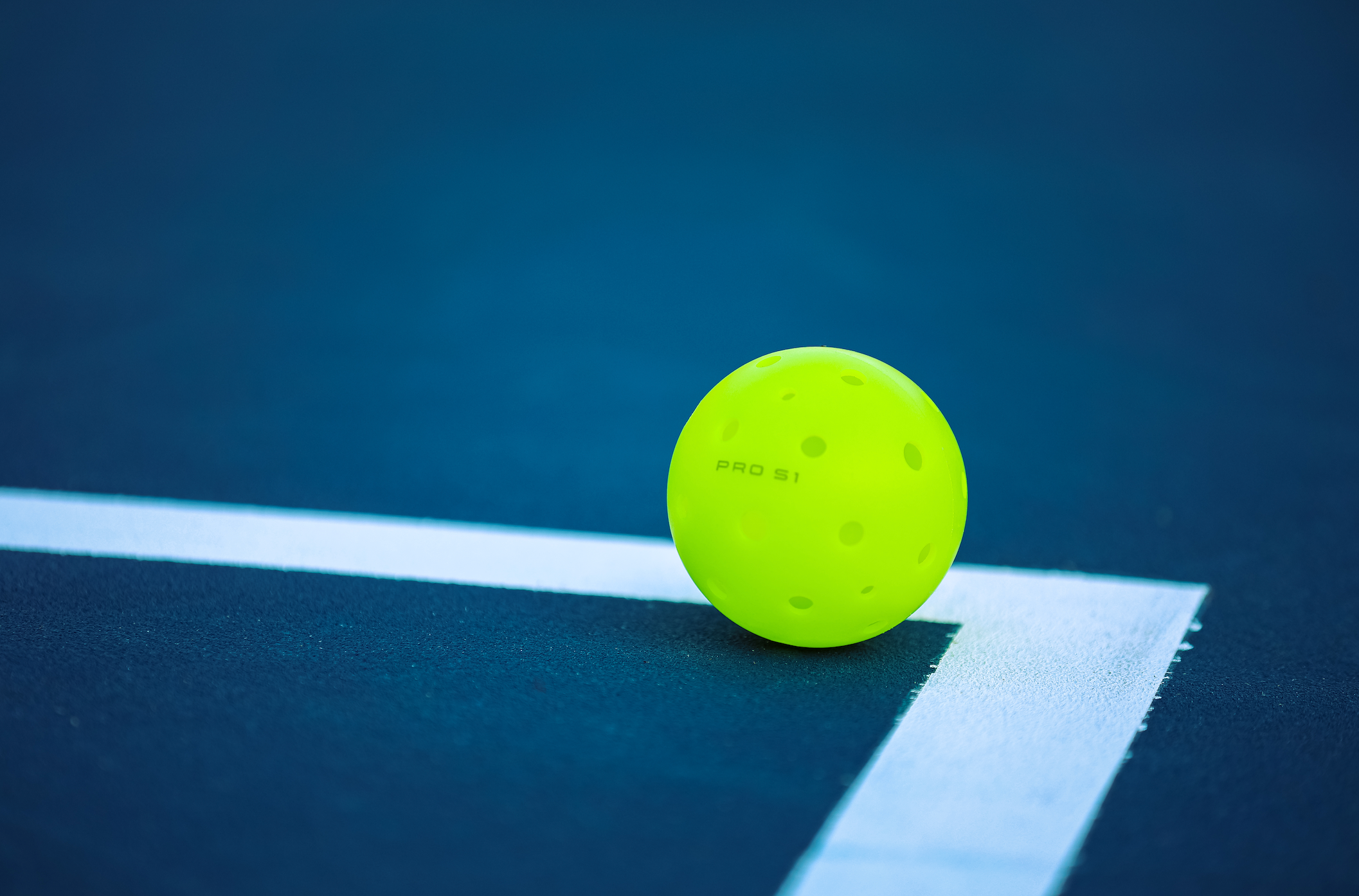 A bright yellow Pro S1 pickleball resting on a court line