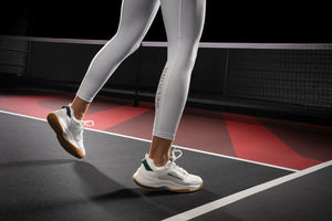 Side view of white pickleball shoes with gum rubber outsole and green heel accent on an indoor court