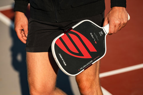 Angled view of Project Boomstik pickleball paddle showing black and red face with Selkirk logo held by a player on an outdoor court