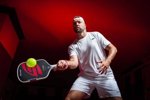Pickleball player hitting a ball with a Project Boomstik paddle in a dramatic red-lit indoor setting
