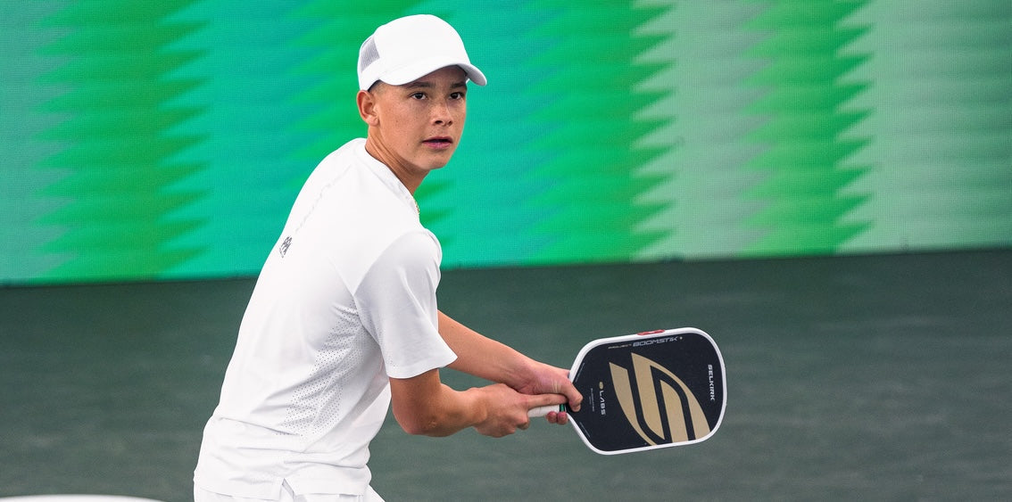 Teen pickleball player preparing a backhand on an indoor court, wearing white and holding a Selkirk paddle