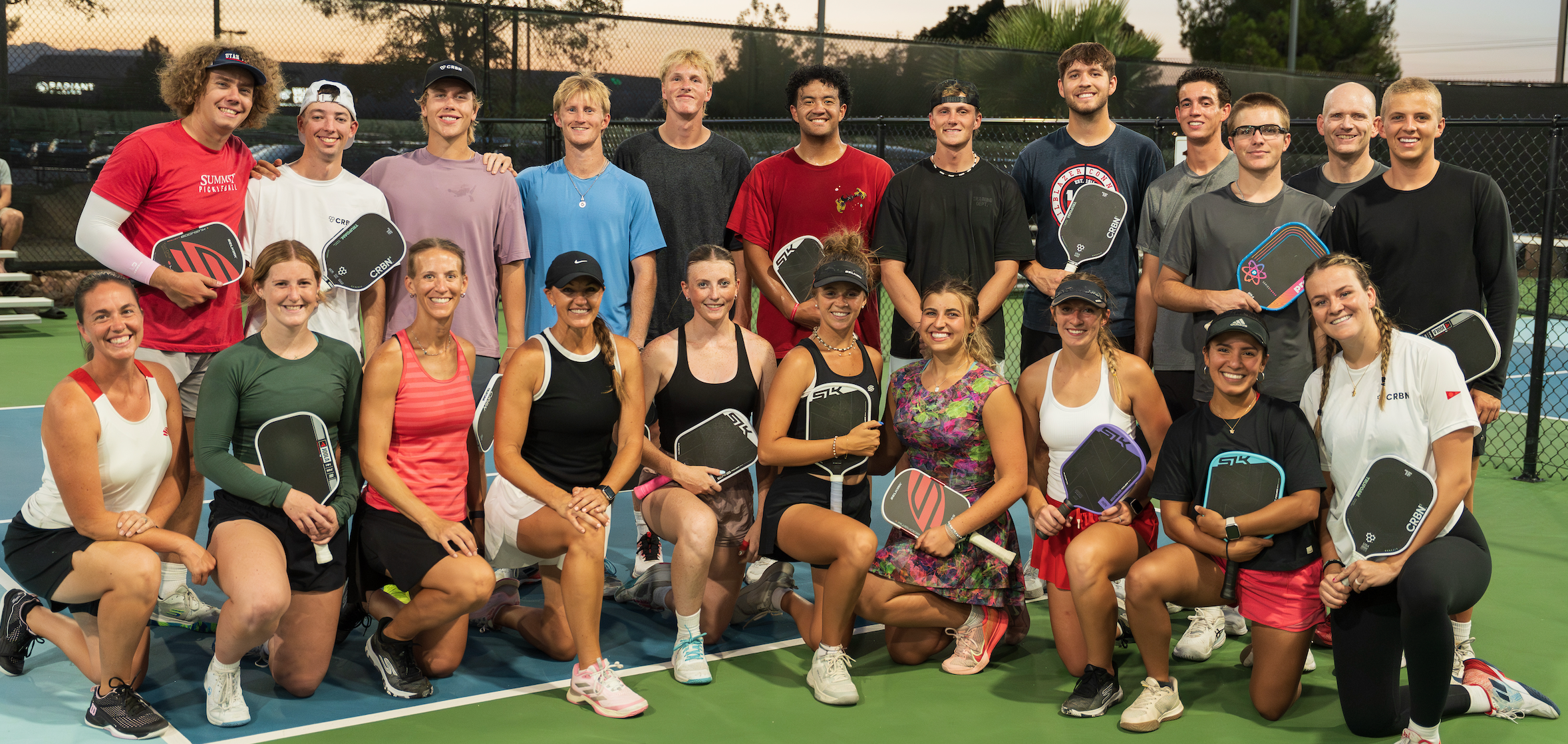 Utah Tech pickleball team posing with paddles on an outdoor court at dusk