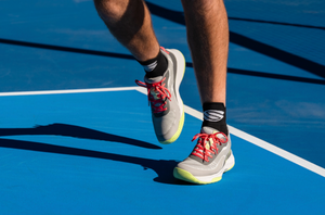A close-up image shows a man's feet in the CourtStrike 2.0 pickleball shoes on an outdoor pickleball court. 