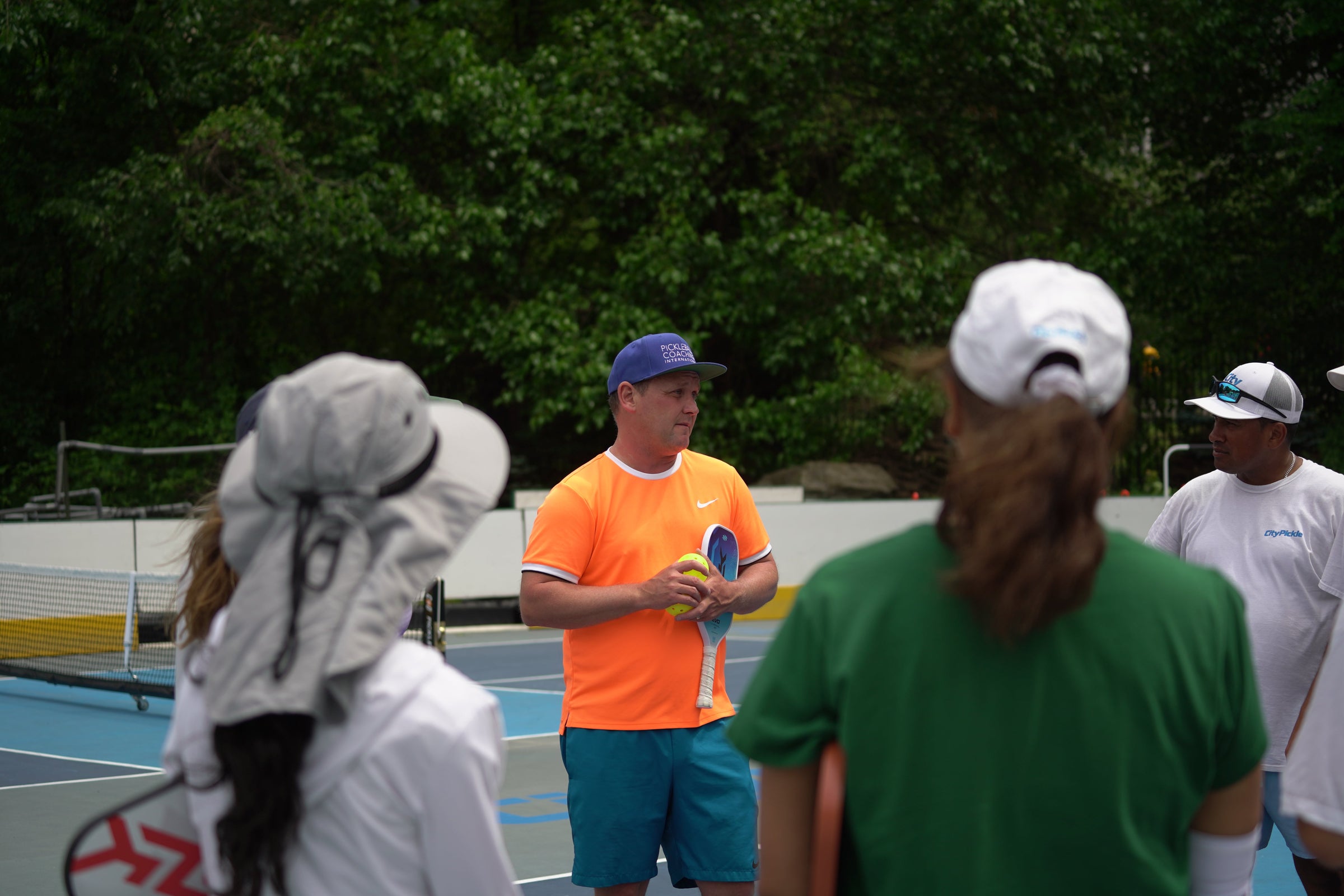 PCI founder Mark Renneson coaches a group of adults on an outdoor pickleball court. 