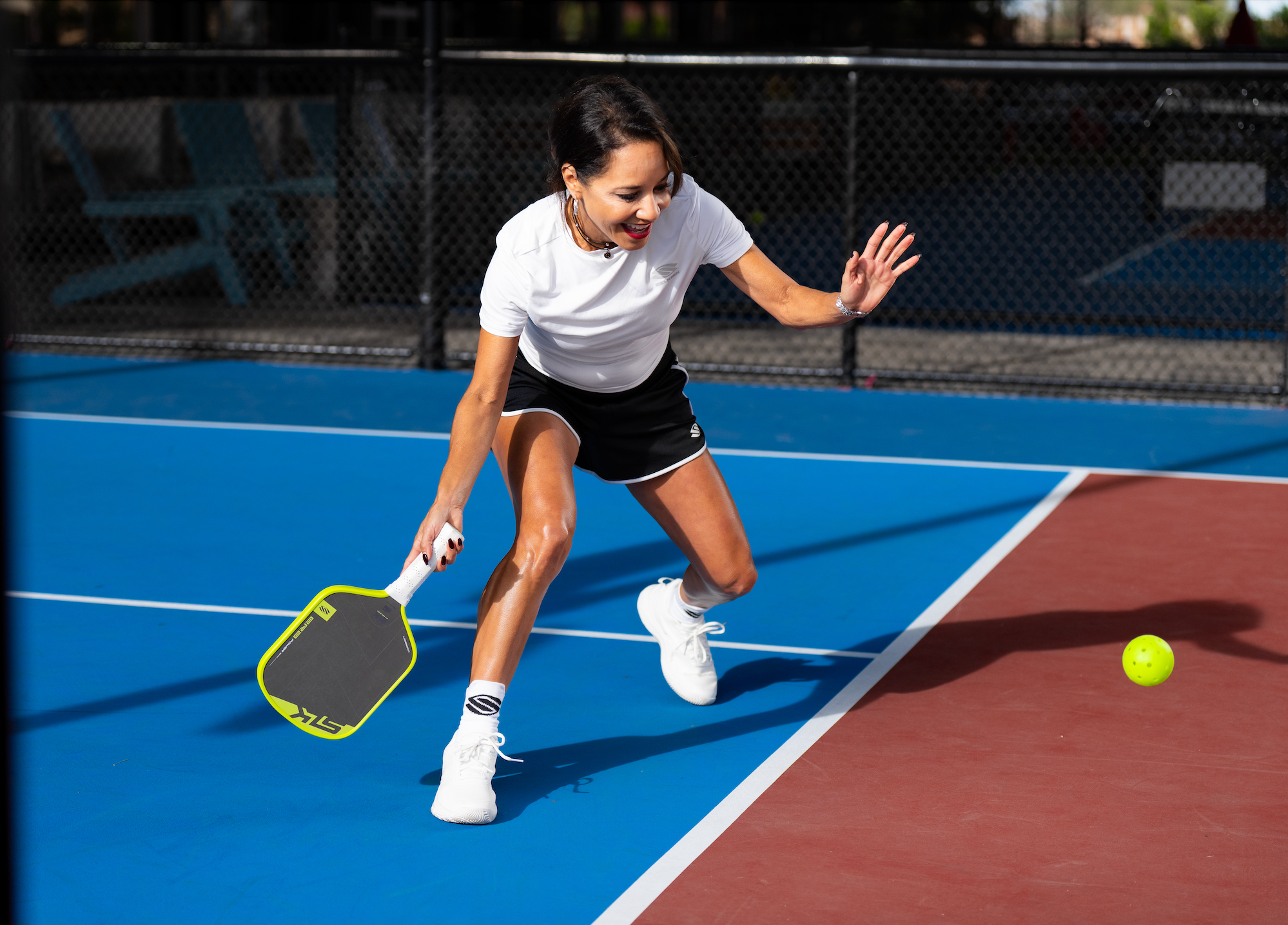 A woman smiles as she prepares to dink a pickleball on an indoor court. 