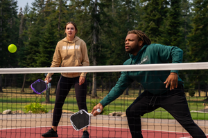 A woman watches as a man prepares to hit a forehand volley. 