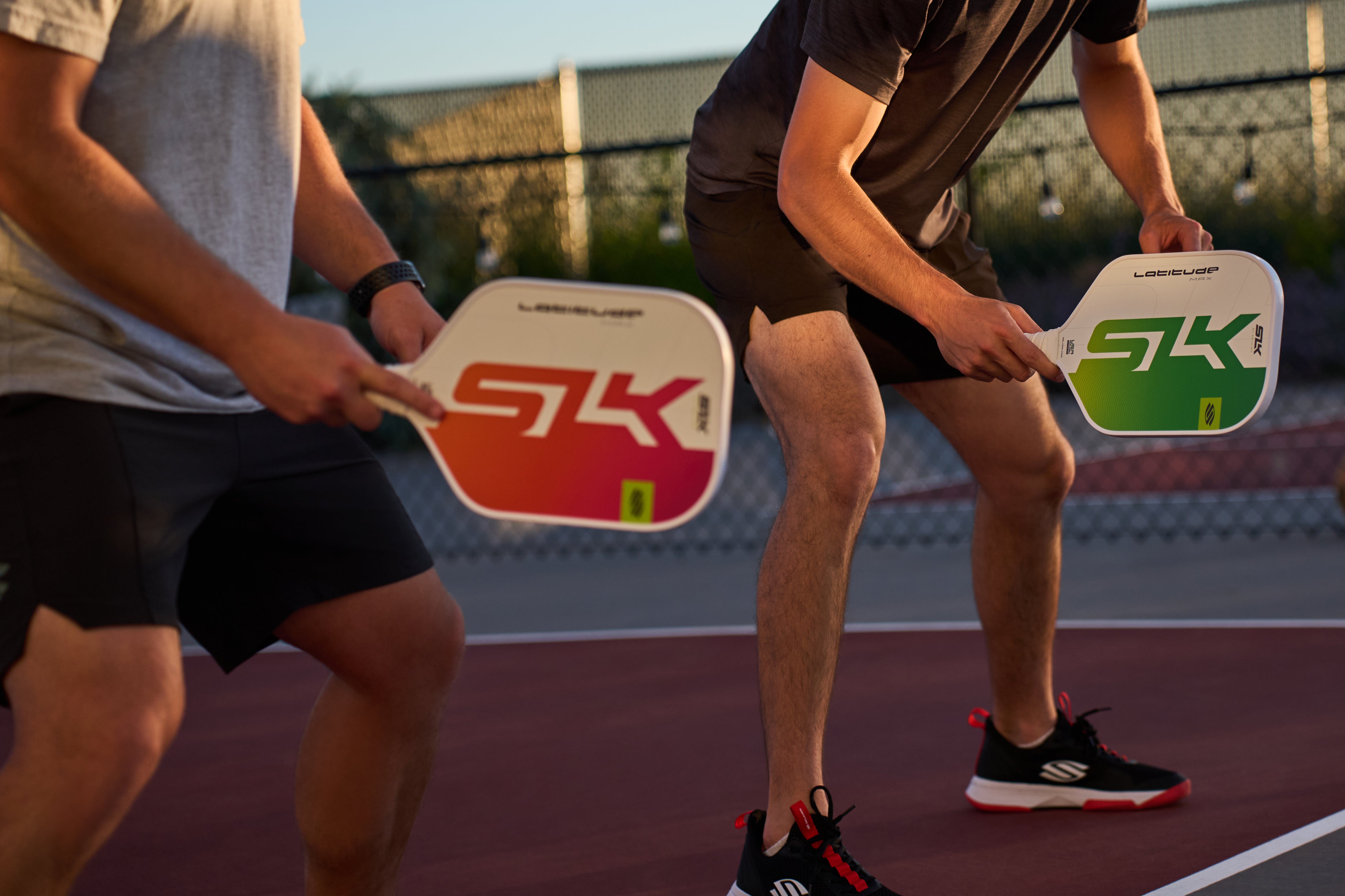 Two men prepare to receive a volley from their opponent as they hold SLK Latitude paddles. 