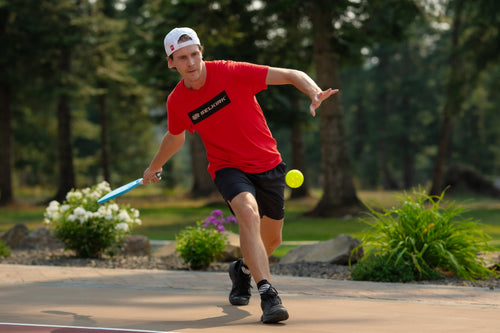 A man drops a pickleball to begin serving. 