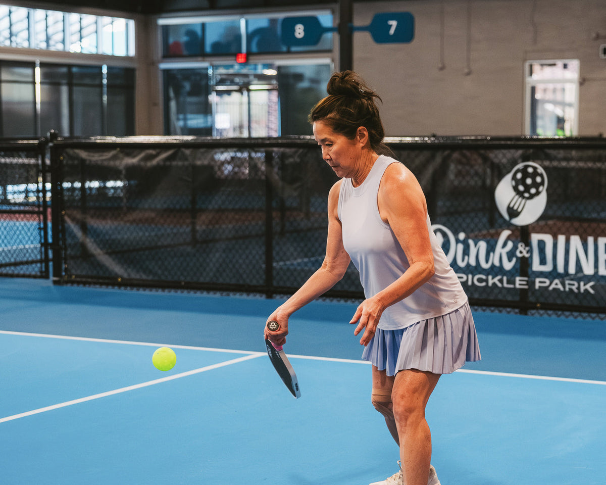 A woman performs a third shot drop from the transition zone of a pickleball court. 