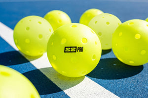 Several Selkirk S2 Pro pickleballs sit on an outdoor pickleball court. 