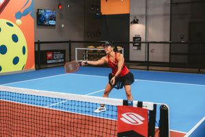 A woman holds her paddle out to perform a volley dink reset. 