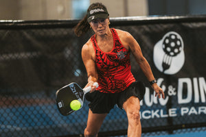 A woman hits a third shot drop with an SLK paddle on an indoor pickleball court. 