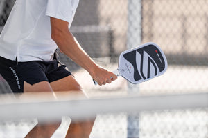 A close-up shows a man's arm as he holds a Selkirk OMNI all-court pickleball paddle. 