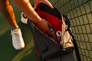 A close-up shows a person pulling a pickleball paddle from the inside of a pickleball bag. 