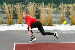 A woman hits a backhand return of serve on an outdoor pickleball court in the snow. 