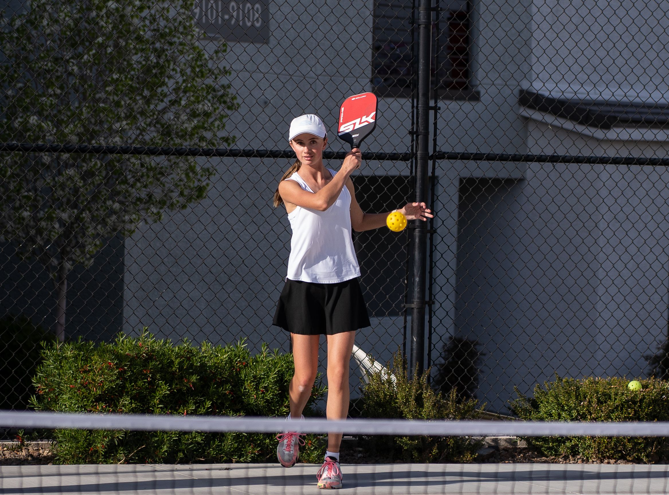 A woman serves a pickleball on an outdoor pickleball court. 