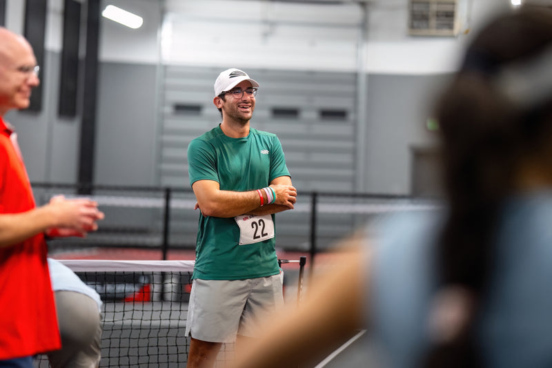 Man in green shirt and white cap standing on a pickleball court with a blurred background