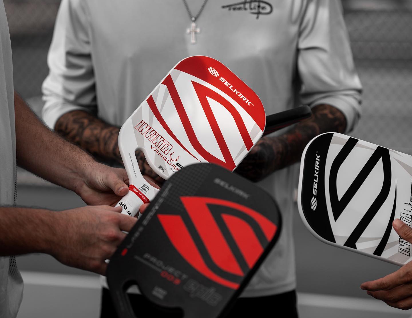 Three Selkirk pickleball paddles being held, featuring black, red, and white designs.