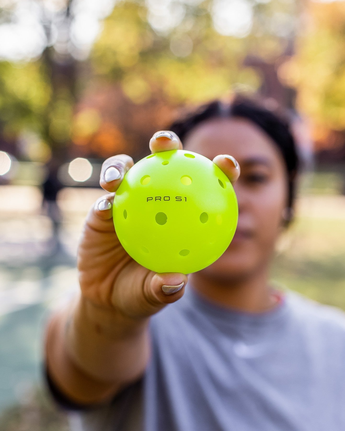 A person holding a bright green Pro S1 pickleball with visible holes and text.
