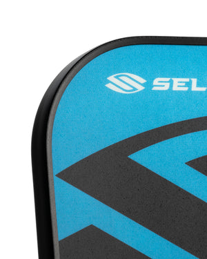 Close-up of blue-and-black board deck pad corner with stylized S logo and text 'SEL'.