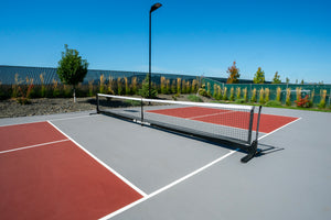 Portable net set up across an outdoor multi-sport court with yellow boundary lines and a white circular center mark