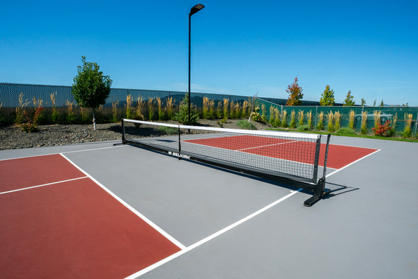Selkirk Semi-Permanent Pro Pickleball Net set up on a court with red playing surface and green background.