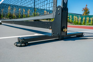 Portable tennis/pickleball net base and upright post with caster wheels on an outdoor court
