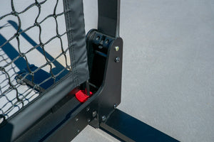 Black net-post hinge and base with red latch, attached net edging on a court surface