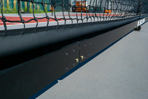 Lower edge of a court net and black metal support beam with bolts on a sports court surface