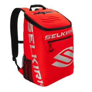 Red backpack with SELKIRK silver logo, top handle, padded shoulder straps, front zip pocket and mesh side pocket.
