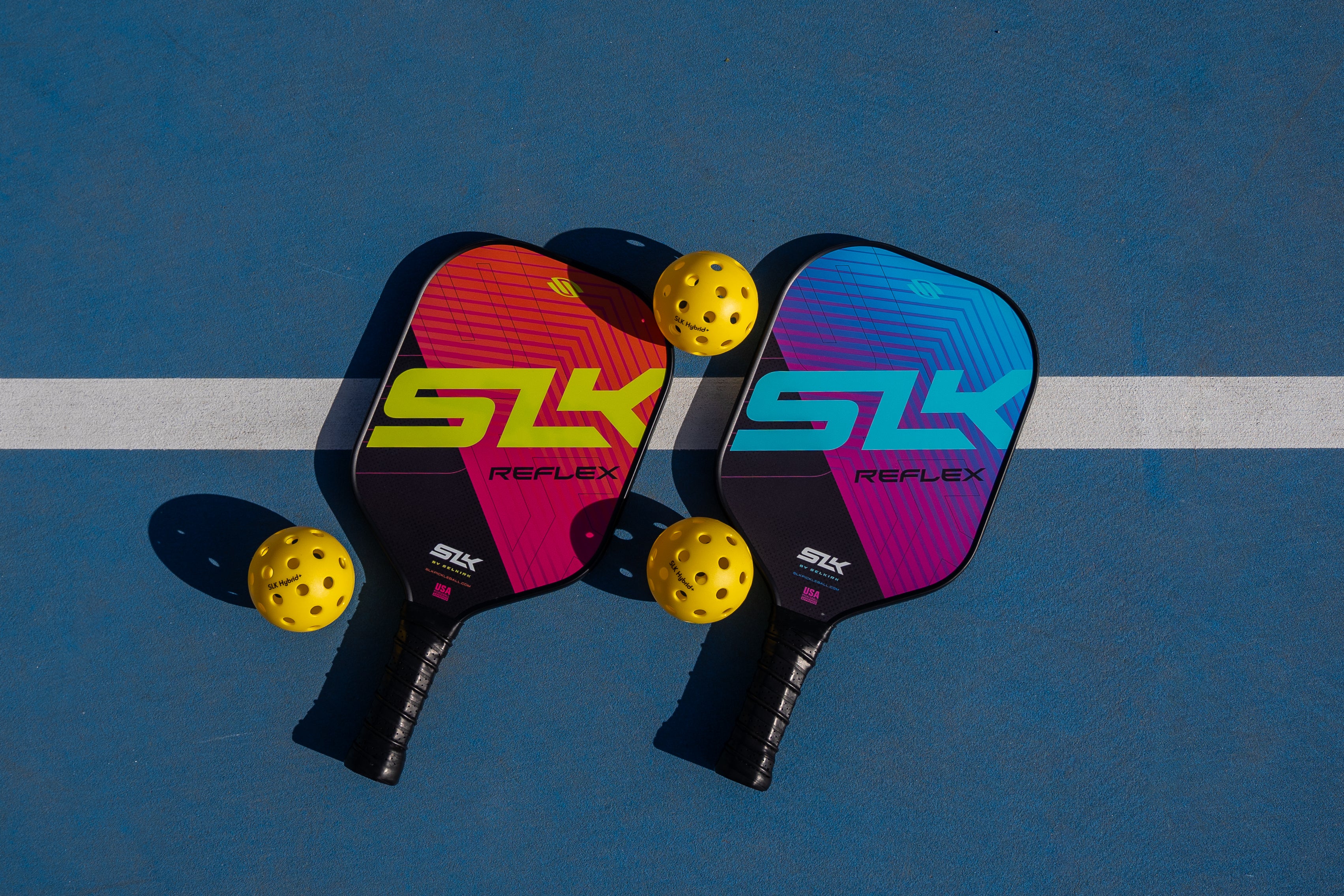 Two SLK Reflex paddles and yellow pickleball balls on a court