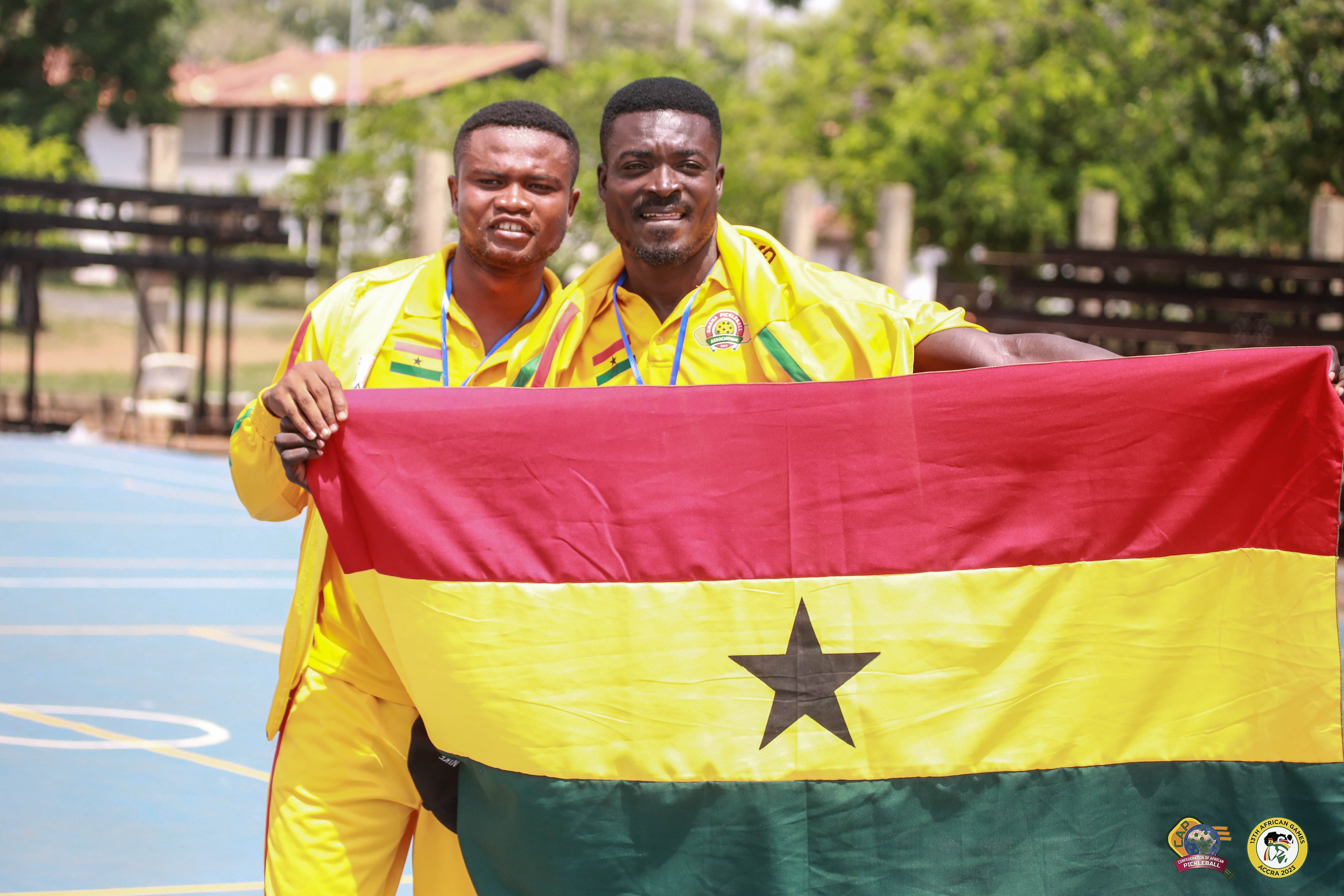 Two athletes in yellow uniforms holding the Ghanaian flag at the 13th African Games.