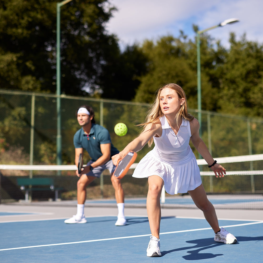 A woman hits a volley with an SLK Halo at an outdoor Invited Club court. 